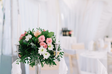 Beautiful wedding floral decoration on a table in a restaurant. White tablecloths, bright room, candles, close-up shooting. The event, happiness, honeymooners. Soft bokeh white background