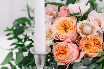 Beautiful wedding floral decoration on a table in a restaurant. White tablecloths, bright room, candles, close-up shooting. The event, happiness, honeymooners. Soft bokeh white background