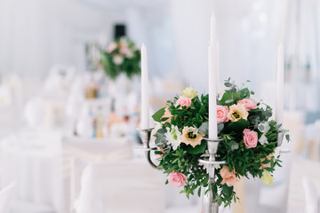 Beautiful wedding floral decoration on a table in a restaurant. White tablecloths, bright room, candles, close-up shooting. The event, happiness, honeymooners. Soft bokeh white background
