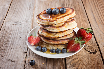  pancakes in a stack with berries and honey on rustic wooden background