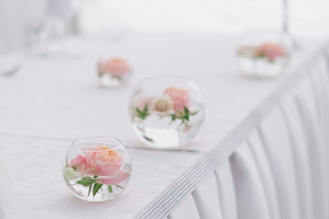 Beautiful wedding floral decoration in glass on a table in a restaurant. White tablecloths, bright room, candles, close-up shooting. The event, happiness, honeymooners. Soft bokeh white background