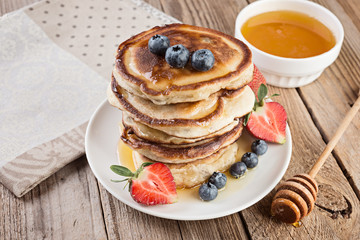  pancakes in a stack with berries and honey on rustic wooden background
