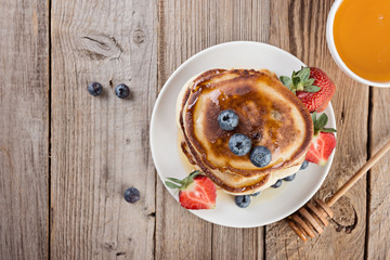  pancakes in a stack with berries and honey on rustic wooden background, top view