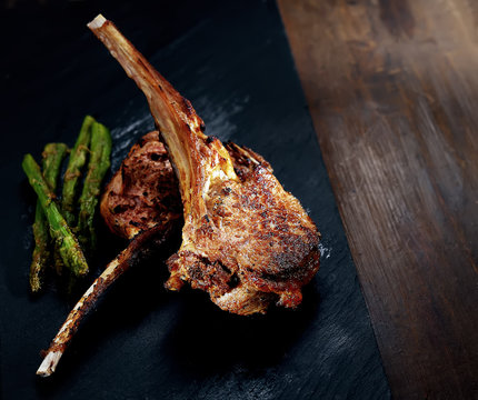 grilled lamb steak with asparagus on a black slate on a wooden background
