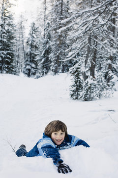 Little boy laying in the snow and smiling while looking at camera