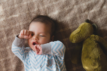 Cute baby boy yawning, lying on blanket with stuffed animal