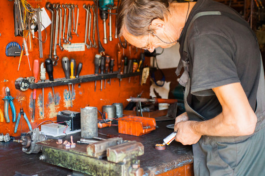 Mechanic putting glue on car parts in his workshop.