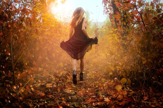 funny girl in black dress running in golden autum forest