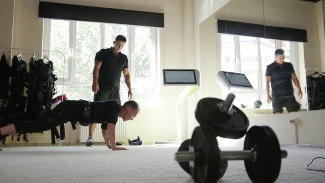 Muscular fitness instructor works with athlete wearing ems suit