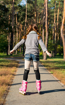 Redhead girl with pigtails skates in the park on rollers