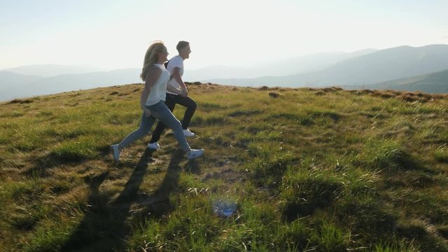Couple jumping on the mountain meadow with arms raised outstretched up.