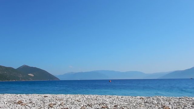A beach with white stone, turquoise sea, blue sky and mountains in background in Ithaca island in Greece. Copy space.
