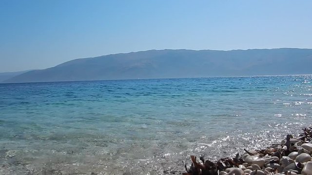 The foreshore with white stone, turquoise sea, blue sky and mountains in background in Ithaca island in Greece. Copy space.