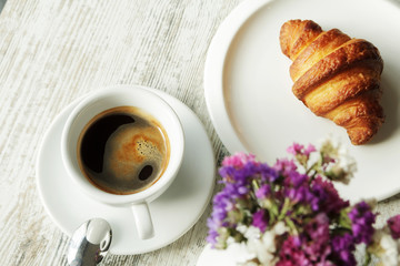 White plate with croissant with cup of fresh black coffee on wooden table. Top view.