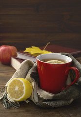 a cup of hot tea with lemon wrapped in a scarf on a wooden table with books in the background