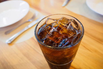 Cola glass soft drink with ice on wood table in restaurant background