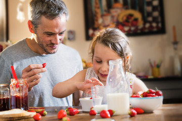 A father and his little girl eating strawberries and sugar