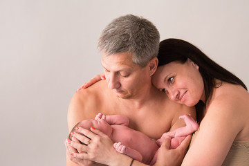 Happy family couple in love on the background. Portrait of happy young family tenderly keeping their sleeping baby on gray background.