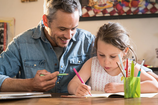 A father helps his little daughter to do her homework for the school.