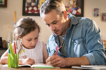 A father helps his little daughter to do her homework for the school. - Powered by Adobe