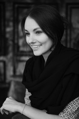 Black and white vertical portrait of young beautiful woman indoor. The girl smiles and does not look at the camera.