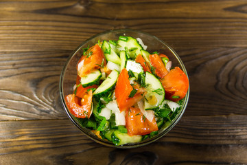 Fresh salad with tomato, cucumber, onion, parsley and dill in glass bowl on wooden table