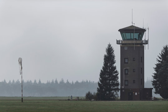 Old air traffic tower in meadow with pine trees.