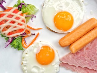 Fried eggs, ham and salad for breakfast on wooden table with copy space.