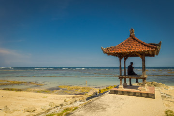 Man wearing a black clothes in a beautiful sunny day under a small cabain in the beach of Pantai pandawa, in Bali island, Indonesia