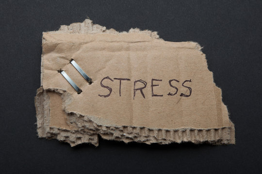 The word "stress" on a torn piece of cardboard box on a black background.