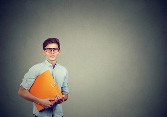 Portrait of young happy smiling man with orange folder isolated on gray background