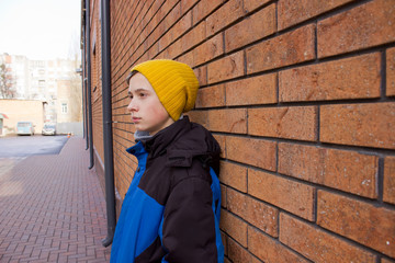 Unhappy Teenage boy standing on the street  near a brick wall