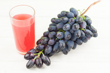 Bunch of fresh ripe blue grapes near transparent and fragile glass full of juice on old wooden rustic white planks