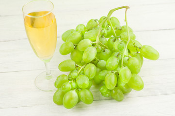 Bunch of fresh ripe green grapes near transparent and fragile glass full of wine on old wooden rustic white planks