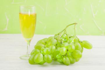 Bunch of fresh ripe green grapes near transparent and fragile glass full of wine on old wooden rustic white planks