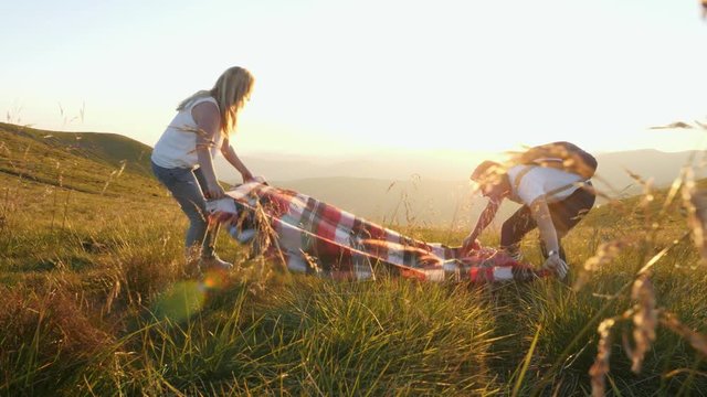 The couple spreads a plaid and sits down on a mountain meadow.
