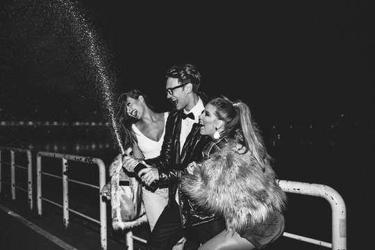 Three friends opening champagne in night out.