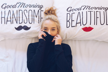 Fototapeta premium Playful woman lying in bed while hiding her face
