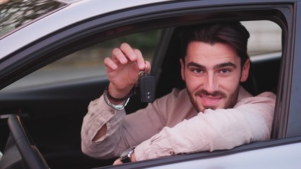 Handsome young man holding bunch of keys, looking in camera, sitting in his new car