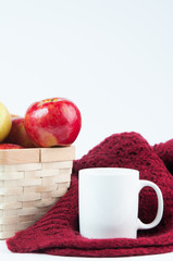 Red apples in a basket with a cozy blanket and mug on a white background