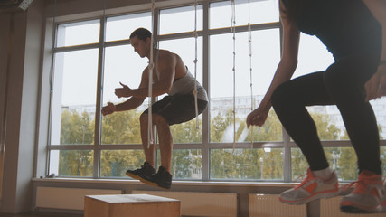 Fototapeta na wymiar Young attractive girl and muscular man fitness instructor doing box jump exercise during a workout at the gym
