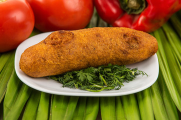 Muchin, an ecuadorian typical food on a white plate with a blurred tomato and pepper behind over a green leaf
