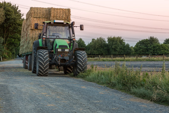 Grüner Traktor mit Anhänger, voll beladen mit Strohballen