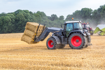 Fototapeta na wymiar Schwarzer Traktor transportiert Strohballen