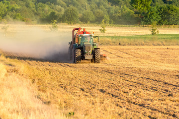 Obraz premium Grüner Traktor mit rotem Anhänger wirbelt eine Staubwolke auf dem Feld auf