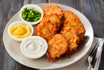 Potato pancakes, latkes or boxty and sauces from sour cream, yogurt, apple sauce and finely chopped green onion on a wooden table of boards