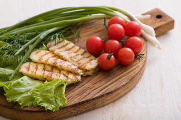 Grilled slices of homemade halloumi cheese with green salad, fresh herbs and organic tomatoes. Fried halloumi cheese with grill marks on wooden background, top view, close-up