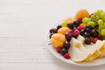 Assortment of juicy fruits on white plate and white table background.. Organic raspberries, apricots, melon, cherries - summer dessert or snack. healthy eating concept.