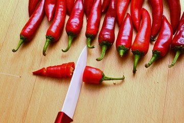 cutting in the kitchen fresh cayenne red hot chili peppers sharp kitchen knife on wooden table