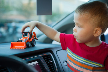 Portrait of cute toddler boy sitting in a car and playing with his plastic tractor. Child holding his toy while being in a car.